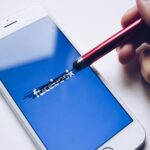 Close-up of a smartphone with a stylus crossing out text on its screen.